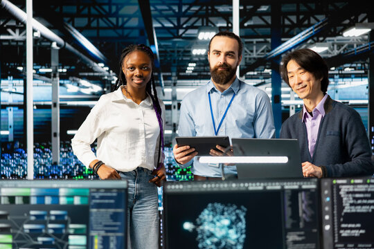 Portrait of multiethnic data center IT team running AI forecasting simulations, tracking performance. Smiling workers in diverse server hub using devices to integrate deep learning APIs