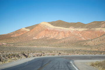 Empty desert highway stretches into hazy mountains under a clear sky
