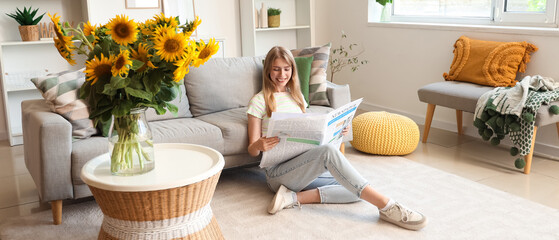Beautiful young happy woman with bouquets of sunflowers reading newspaper at home
