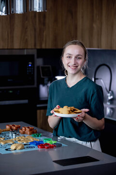 A joyful young girl is happily holding a plate full of freshly baked cookies in a modern kitchen setting