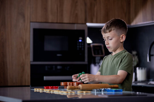 Little boy making cookies using cookie cutters and dough in the kitchen at home