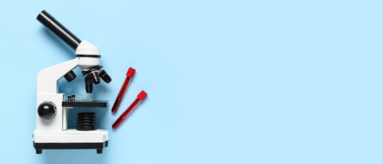Microscope and test tubes with blood samples on blue background with space for text