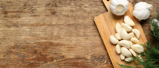 Cutting board with fresh garlic cloves and dill on wooden background