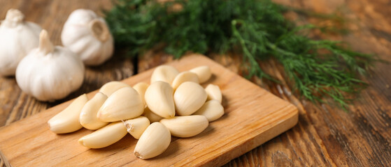 Cutting board with fresh garlic cloves and dill on wooden background, closeup