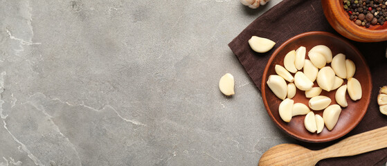 Wooden plate with fresh garlic cloves and bowl of peppercorns on grey background