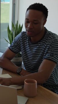 Vertical video: Glancing out window, man is typing and jotting notes on laptop to complete report