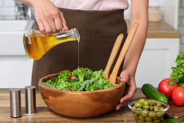 Woman adding olive oil into bowl with tasty salad at table in kitchen