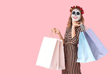 Young woman with painted skull and shopping bags on pink background. Mexico's Day of the Dead (El...