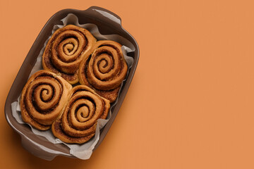 Baking dish of tasty cinnamon rolls on brown background