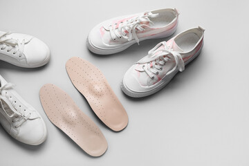Pair of orthopedic insoles and stylish female shoes on light background