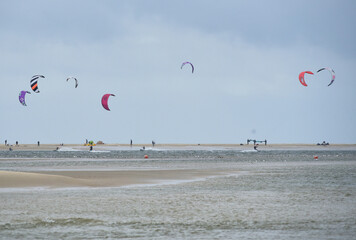 Colorful kites rise above the North Sea as kitesurfers glide across the water on Borkum beach. A typical scene of water sports in the Wadden Sea.