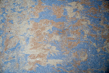 Close-up of a rough granular surface with natural blue, tan, and rust-colored textures forming an abstract pattern. Suitable for use as a background or design texture.
