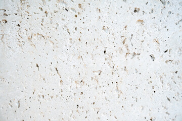 Close-up of a white stone wall surface with natural pits, holes, and weathered textures. Suitable as a background or abstract texture.