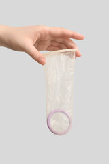 Female hand with open condom on grey background, closeup