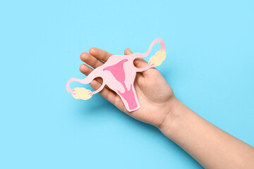 Female hand with paper uterus on color background, closeup