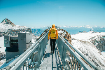 Solo Hiker in Yellow Jacket with Yellow Backpack Crossing Suspension Bridge at Glacier 3000, Switzerland