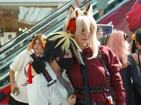 Two people dressed in anime costumes embrace each other at a celebration. They demonstrate their friendly relationship amidst the bustling event,