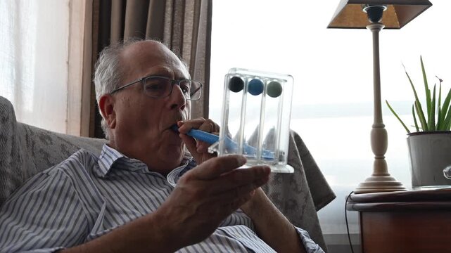 Retired man using a spirometer at home blowing through a tube to measure and strengthen his lungs after a respiratory illness
