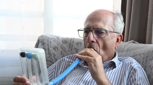 Elderly man blowing vigorously into a spirometer to exercise and strengthen his lungs after recovering from a respiratory illness