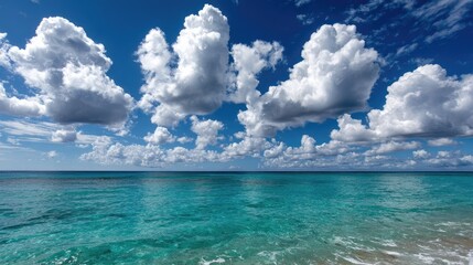 Obraz premium A stunning coastal view showcasing clear turquoise waters meeting a vibrant blue sky filled with fluffy white clouds. Perfect for summer vibes and relaxation imagery.