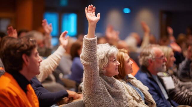 A senior woman raises her hand to ask a question or vote during a town hall meeting or conference. Represents civic engagement, democracy, and community participation