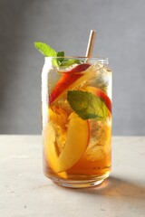 Refreshing iced peach tea with mint in glass on white table, closeup