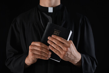 Priest with Holy Bible on black background, closeup