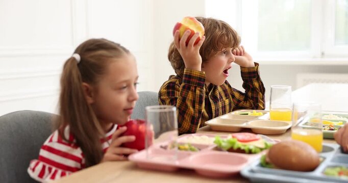 Little kids eating lunch at wooden table in school canteen