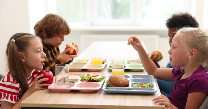 Little kids eating lunch at wooden table in school canteen