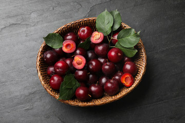 Ripe cherry plums and green leaves in wicker basket on dark textured table, top view