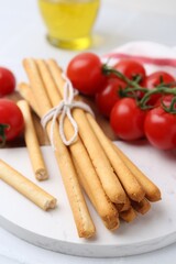 Delicious grissini sticks and fresh tomatoes on white table, closeup
