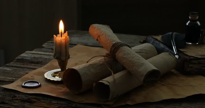 Old rolled scrolls and burning candle on wooden table, closeup