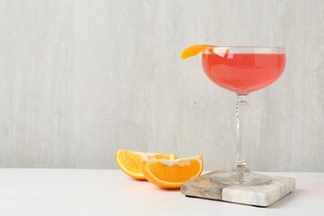Martini cocktail with garnish and slices of orange on white table, space for text