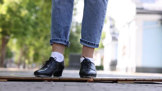 Teenage girl in tap shoes dancing outdoors, closeup. Camera moving right