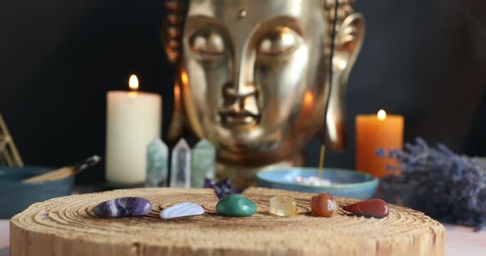 Chakra gemstones on table with burning candles, incense, palo santo, lavender flowers and Buddha figure, closeup