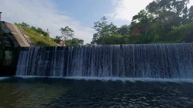 Water dam view in tropical countryside with bridge built structure. Beautiful waerfall face with blue sky background