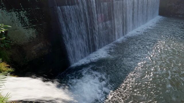 Water dam view in tropical countryside with bridge built structure. Tilting up camera movement and reveal of waterfall