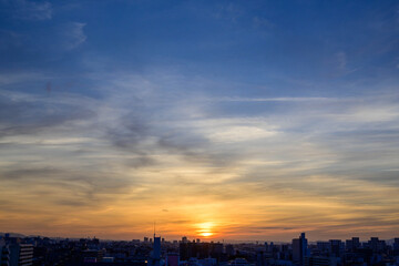 神戸市の夜明け、ビルの隙間から太陽が昇り辺りはオレンジ色に染まりビルはシルエットに浮かぶ。