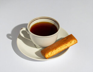 a single cup of hot tea with a biscotti cookie on a white saucer with shadows