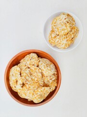 Tempeh chips in a small white plate and a wooden plate on a white background. Top of view. 