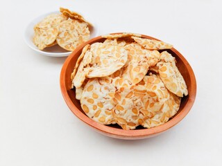 Tempeh chips in a small white plate and a wooden plate on a white background. High angle view. 