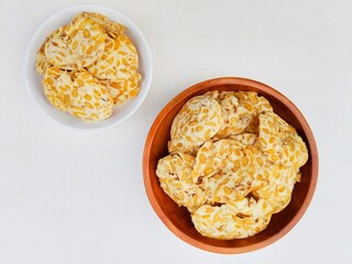 Tempeh chips in a white plate and a wooden plate on a white background. Top of view. 
