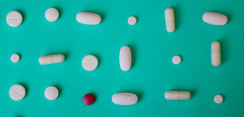 White pills, capsules, and one red pill are arranged in neat rows on a turquoise background, reminiscent of a sea wave. This minimalist and ordered shot highlights themes of health, pharmaceuticals, a