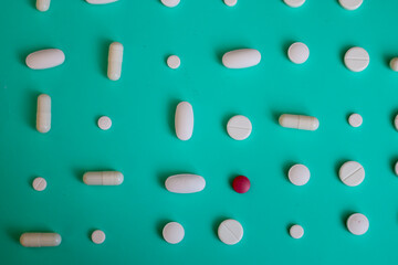 White pills and capsules, along with one red pill, are arranged on a vibrant turquoise background, symbolizing medicine and pharmaceuticals. This ordered composition of various shapes creates a visual