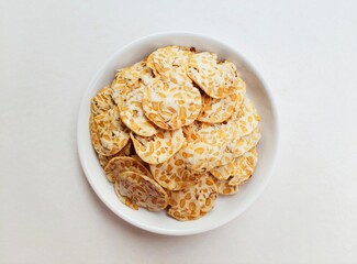 Tempeh chips in a white plate on a white background. Top of view. 