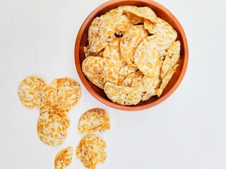 Tempeh chips in a wooden plate on a white background. Top of view. 