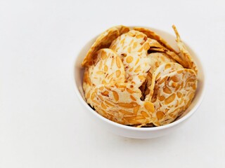 Tempeh chips in a white bowl on a white background. 