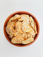 Tempeh chips in a wooden plate on a white background. Top of view. 