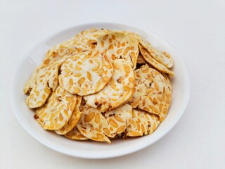 Tempeh chips in a white plate on a white background. High angle view. 