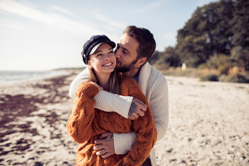 Happy couple hugging on beach in autumn clothes